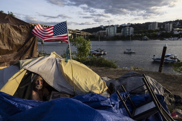 FILE - Frank, a homeless man, sits in his tent with a river view, June 5, 2021, in Portland, Ore. Momentum is building in a case regarding homeless encampments before the U.S. Supreme Court that could have major implications for cities as homelessness nationwide has reached record highs. (AP Photo/Paula Bronstein, File)
