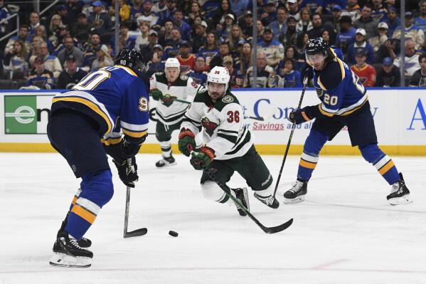 Minnesota Wild's Mats Zuccarello (36) lunges for the puck between St. Louis Blues' Ryan O'Reilly (90) and Brandon Saad (20) during the second period in Game 3 of an NHL hockey Stanley Cup first-round playoff series Friday, May 6, 2022, in St. Louis. (AP Photo/Michael Thomas)