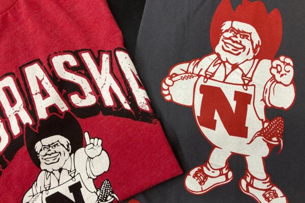 Nebraska Huskers t-shirts featuring new cartoon mascot Herbie Husker, left, and old cartoon mascot, right, are displayed at the Husker Hounds store in Omaha, Neb., Saturday, Jan. 29, 2022. The University of Nebraska-Lincoln has made a change to its cartoon mascot Herbie Husker to eliminate confusion about the meaning of a hand gesture he makes that some people connect with white supremacy.(AP Photo/Eric Olson)