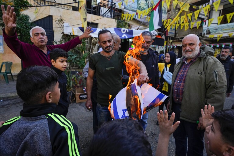 Palestinians burn Israeli flags, during the observance of a global day of boycotts and strikes called for by pro-Palestinian activists to demand a cease-fire in Gaza, at Bourj al-Barajneh Palestinian refugee camp in Beirut, Lebanon, Monday, Dec. 11, 2023. Public agencies, schools and banks were shuttered in Lebanon Monday in observance of a global day of boycotts and strikes called for by pro-Palestinian activists to demand a ceasefire in Gaza. (AP Photo/Bilal Hussein)