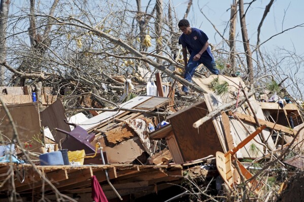 Family friend Trey Bridges, 16, climbs a mountain of tornado debris to help the Blansett family recover items not destroyed by Saturday's tornado, Sunday, March 16, 2025, in Tylertown, Miss. (AP Photo/Rogelio V. Solis, File)