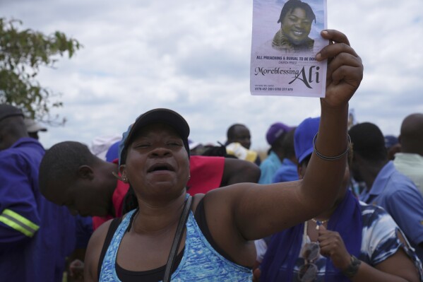 A woman holds a flyer with a portrait of Moreblessing Ali, at her burial on the outskirts of Harare, Saturday, March, 2, 2024. A Zimbabwean activist slain two years ago was finally laid buried Saturday at a low key but tension filled event where tensions among party members betrayed the state of the country once promising opposition, which appears collapsing under the weight of infighting and allied state repression. (AP Photo/Tsvangirayi Mukwazhi)