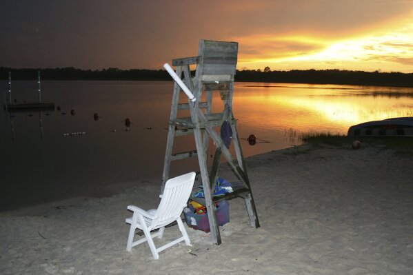 In this undated photo released by Camp Kiwanis, a lifeguard chair stands as the sun sets on Mill Dam Lake in the Ocala National Forest, where Camp Kiwanis has hosted local children since 1948 near Ocala, Fla. Camp Kiwanis will not open this summer for the first time in 72 years due to concerns about spread of the novel coronavirus. Camps across the U.S. are scrambling to make a similar decision about summer 2020 and parents are getting a first wave of closure notices for some camps in harder-hit states. (Scott Mitchell/Camp Kiwanis via AP)