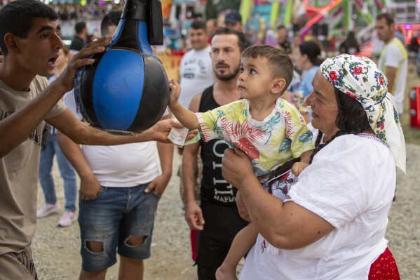 A child tries to punch a boxing arcade machine at a fair in Hagioaica, Romania, Thursday, Sept. 14, 2023. For many families in poorer areas of the country, Romania's autumn fairs, like the Titu Fair, are one of the very few still affordable entertainment events of the year. (AP Photo/Alexandru Dobre)