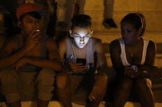 FILE - In this July 1, 2015 file photo, youths use a password protected wifi network coming from a five star hotel to surf the Internet on their smart phones in downtown Havana, Cuba. Cuba's government announced on Tuesday, Dec. 4, 2018 that its citizens will be offered full internet access on mobile phones starting Thursday, Dec. 6, becoming one of the last nations to do so. (AP Photo/Desmond Boylan, File)