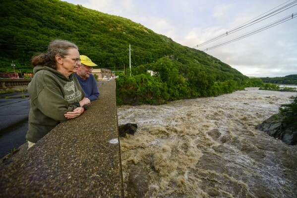 People stand on the Vilas Bridge, in Bellows Falls, Rockingham, Vt., to watch the water from the Connecticut River flow through on Monday, July 10, 2023. Heavy rain has washed out roads and forced evacuations in the Northeast, especially in Vermont and New York. (Kristopher Radder/The Brattleboro Reformer via AP)