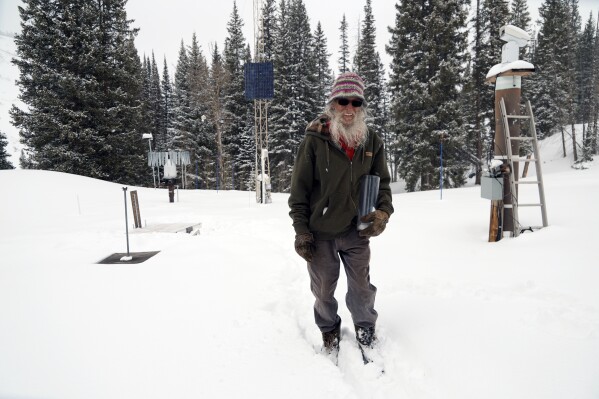 Billy Barr holds his canister with newly fallen snow Wednesday, March 13, 2024, in Gothic, Colo. So-called “citizen scientists” like Barr have long played important roles in gathering data to help researchers better understand the environment. His once hand-recorded measurements have informed numerous scientific papers and helped calibrate aerial snow sensing tools. (AP Photo/Brittany Peterson)