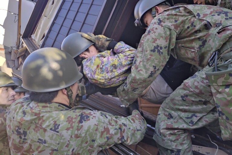 In this photo provided by Japanese Ministry of Defense, Japanese Self Defense Force members carry an injured person out of a collapsed house, following strong earthquakes in Wajima, Ishikawa prefecture, Japan, Tuesday, Jan. 2, 2024. (Japanese Ministry of Defense via AP)