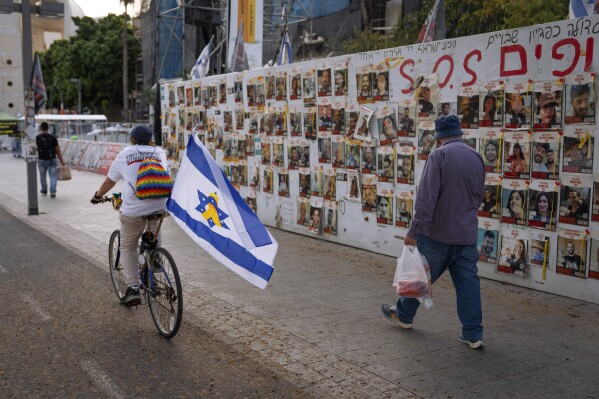 Passersby observe the photos of hostages held in the Gaza Strip that are plastered to the walls of a plaza known as Hostages Square in Tel Aviv, Israel, Friday, May 17, 2024. (AP Photo/Oded Balilty).