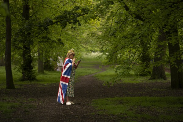 A woman draped in a British flag smokes during the Big Lunch celebrations in London Regent's Park, on May 7, 2023. The Big Lunch was part of the weekend of celebrations for the Coronation of King Charles III. (AP Photo/Vadim Ghirda)