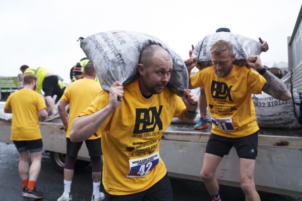 A contestant loads a 50kg bag of coal onto his shoulders during the men's open category at the World Coal Carrying Championships in Ossett, West Yorkshire, England, Monday, April 21, 2025. (AP Photo/Jon Super)