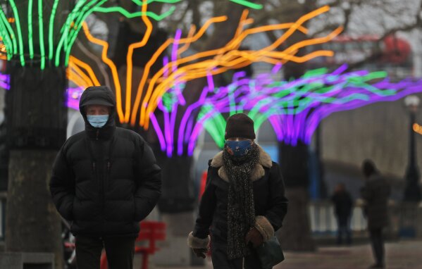A couple wear face coverings as they stroll past illuminated trees on the Southbank in London, Friday, Jan. 8, 2021. Britain's Prime Minister Boris Johnson has ordered a new national lockdown for England which means people will only be able to leave their homes for limited reasons, with measures expected to stay in place until mid-February. (AP Photo/Frank Augstein)