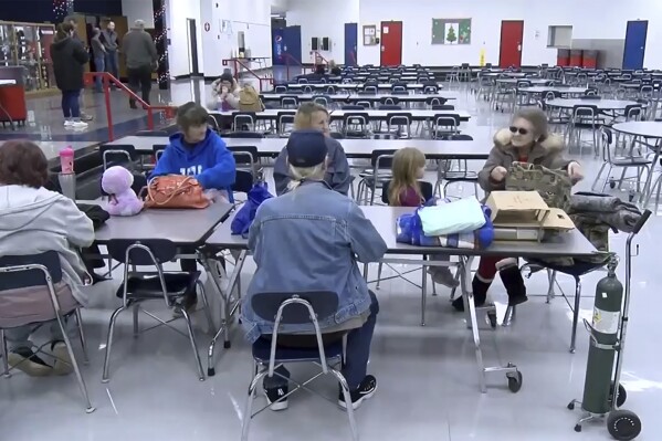 This image taken from video and provided by WTVQ shows people sitting at a table at Rockcastle Middle School being used as an evacuation center in Mt Vernon, Ky., Wednesday, Nov. 22, 2023. People were evacuated from a nearby town after a CSX train derailed Wednesday near Livingston, a remote town with about 200 people in Rockcastle County. CSX says two of the 16 cars that derailed carried molten sulfur, which caught fire after the cars were breached. (WTVQ via AP)