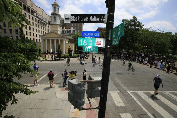With St. John's Church in the background, people walk under a new street sign on Friday, June 5, 2020, in Washington. "The section of 16th street in front of the White House is now officially 'Black Lives Matter Plaza,'" District of Columbia Mayor Muriel Bowser tweeted. The black and white sign was put up to mark the change. (AP Photo/Manuel Balce Ceneta)
