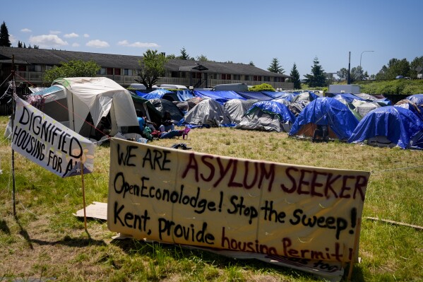 Varios letreros que piden ayuda se encuentran frente a un campamento de solicitantes de asilo provenientes en su mayoría de Venezuela, Congo y Angola, junto a un motel desocupado propiedad del condado, el miércoles 5 de junio de 2024, en Kent, Washington. (AP Foto/Lindsey Wasson)