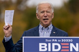 Democratic presidential candidate former Vice President Joe Biden holds up his daily schedule which has a daily update on US Troop deaths and wounded numbers as he speaks at a drive-in campaign stop at Bucks County Community College in Bristol, Pa., Saturday, Oct. 24, 2020. (AP Photo/Andrew Harnik)