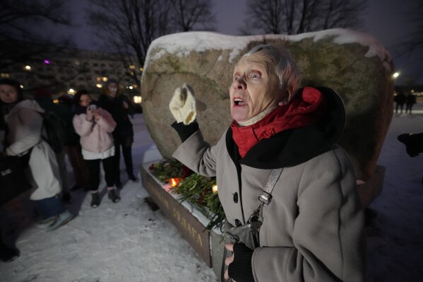 Lyudmila, 83, addresses people who gathered to lay flowers to pay their respect to jailed Russian opposition leader Alexei Navalny, who has died in a Russian prison, according to the Federal Penitentiary Service, at the monument, a large boulder from the Solovetsky islands, where the first camp of the Gulag political prison system was established, in St. Petersbiurg, Russia on Friday, Feb. 16, 2024. (AP Photo/Dmitri Lovetsky)