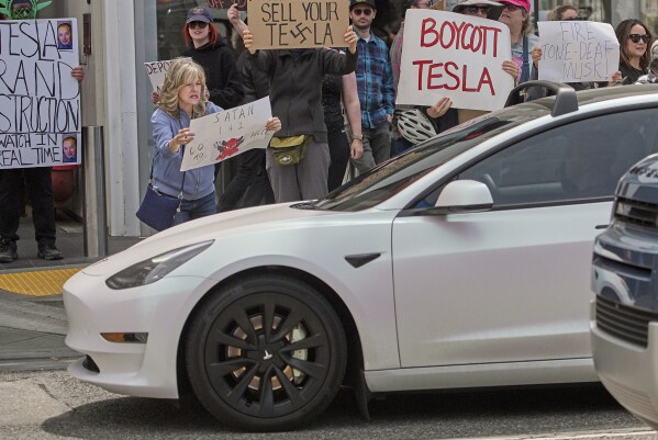 Protesters rally during a protest outside a Tesla showroom against U.S. President Donald Trump and Tesla CEO Elon Musk outside a Tesla showroom in Santa Monica, Calif., on Saturday, March 29, 2025. (AP Photo/Damian Dovarganes)