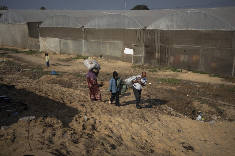 Des membres de la famille Abu Jarad, déplacés par le bombardement israélien de la bande de Gaza, portent des sacs remplis de bois et de feuilles d'arbres sèches dans un camp de tentes de fortune dans la région de Muwasi, au sud de Gaza, le lundi 1er janvier 2024. ( AP Photo/Fatima Chbaïr)
