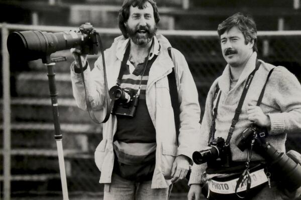 Former Associated Press photographer Jack Smith, left, is seen with fellow photographer Steven Nehl, then of the Oregonian newspaper, during an NCAA college football game in Eugene, Ore., in the early 1990s. Jack Smith, an AP photographer who captured unforgettable shots of the eruption of Mount St. Helens, the Exxon-Valdez oil spill, the Olympics and many other events during his 35-year career with the news organization, passed away on Jan. 4, 2023, at his home in La Mesa, Calif. He was 80. (Greg Wahl-Stephens via AP)