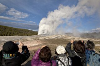 FILE - In this May 21, 2011, file photo, tourists photograph Old Faithful erupting on schedule late in the afternoon in Yellowstone National Park, Wyo. A woman has suffered burns after falling into a thermal feature at Yellowstone National Park, which is closed because of the coronavirus pandemic. Officials say she was reportedly backing up while taking photos Tuesday, May 12, 2020, and fell into a hot spring or hole where hot gases emerge near Old Faithful geyser. (AP Photo/Julie Jacobson, File)