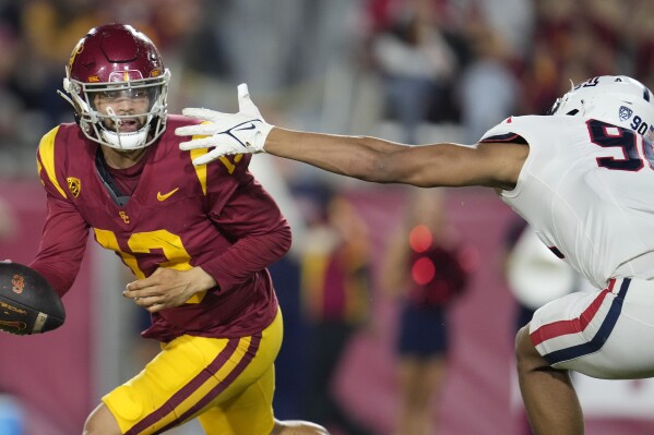 Southern California quarterback Caleb Williams, left, evades the tackle attempt by Arizona defensive lineman Isaiah Ward during the first half of an NCAA college football game Saturday, Oct. 7, 2023, in Los Angeles. (AP Photo/Marcio Jose Sanchez)