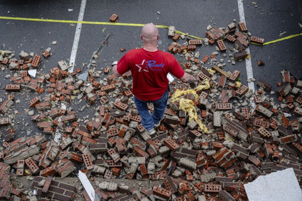 A person walks over the fallen brick facade from the front of a damaged business in the Triad Building, a business plaza, after severe weather passed through Thursday, April 3, 2025, in Louisville, Ky. (AP Photo/Jon Cherry)