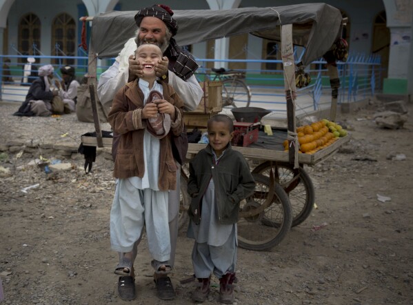 FILE - A fruit seller lifts his son by his cheeks in the center of Kandahar, Afghanistan, March 12, 2014. (AP Photo/Anja Niedringhaus, File)