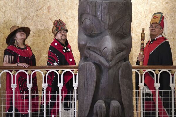 Earl Stephens, who has the Nisga'a cultural name Chief Ni'is Joohl, centre left, with Pamela Brown, left and another member of the delegation from the Nisga'a nation pose beside the 11-metre tall memorial pole, during a visit to the National Museum of Scotland, ahead of its return to what is now British Columbia, in Edinburgh, Monday, Aug. 28, 2023. Members of a Canadian First Nation held a spiritual ceremony on Monday at a Scottish museum to begin the homeward journey of a totem pole stolen almost a century ago. (Andrew Milligan/PA via AP)