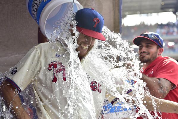 Philadelphia Phillies starting pitcher Zack Wheeler is doused with water in the dugout by teammates Zack Eflin, right and Aaron Nola, rear, after a victory against the New York Mets, Sunday, Aug. 8, 2021, in Philadelphia. The Phillies won 3-0. (AP Photo/Derik Hamilton)