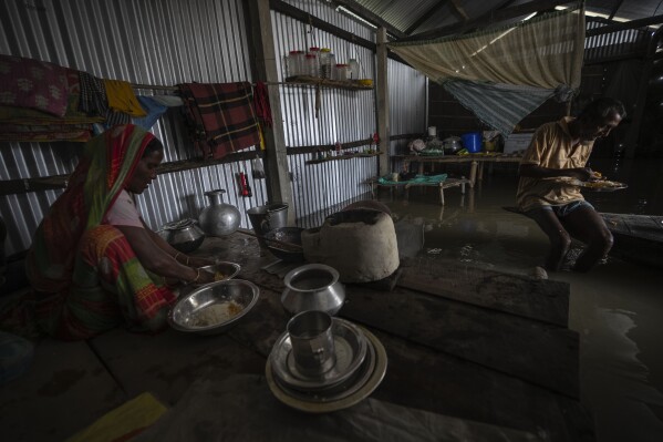 Yaad Ali, 55, right, and his wife Monuwara Begum, 45, eat a meal in their submerged house in Sandahkhaiti, a floating island village in the Brahmaputra River in Morigaon district, Assam, India, Wednesday, Aug. 30, 2023. (AP Photo/Anupam Nath)