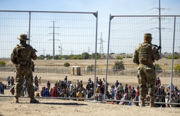 FILE - Migrants wait in line adjacent to the border fence under the watch of the Texas National Guard to enter into El Paso, Texas, May 10, 2023. Senators are racing to release a highly-anticipated bill that pairs border enforcement policy with wartime aid for Ukraine, Israel and other U.S. allies, as part of a long-shot effort to push the package through heavy skepticism from Republicans, including House Speaker Mike Johnson. (AP Photo/Andres Leighton)