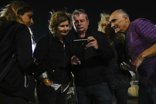 People look at the news showing the Israeli hostages released by Hamas from the Gaza strip, in Tel Aviv, Israel, on Sunday, Nov. 26, 2023. (AP Photo/Ariel Schalit)