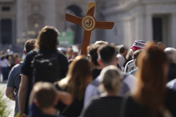 Pilgrims carrying a cross make their way to the Holy Door in St. Peter's Square at the Vatican after Cardinal Camerlengo Kevin Joseph Farrell announced the death of Pope Francis, Monday, April 21, 2025. (AP Photo/Andrew Medichini)