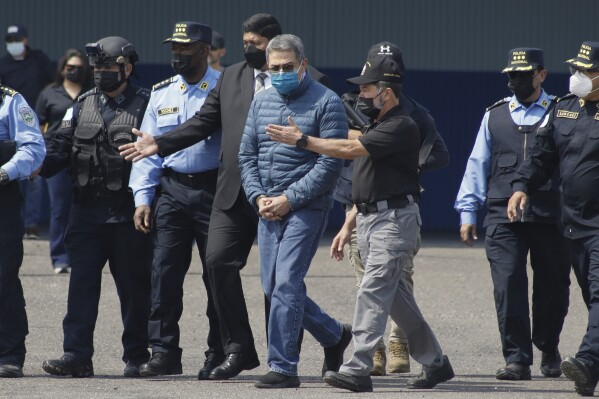 FILE - Former Honduran President Juan Orlando Hernandez, center, is taken in handcuffs to a waiting aircraft as he is extradited to the United States to face drug trafficking charges at an Air Force base in Tegucigalpa, Honduras, April 21, 2022. Hernandez's trial in New York starts Monday, Feb. 12, 2024. (AP Photo/Elmer Martinez, File)