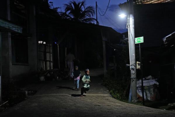 A boy runs under a street light on Karampuang Island whose electricity relies on solar power plants, in West Sulawesi, Indonesia, Thursday, Dec. 22, 2022. While Indonesia has vast renewable and green energy potential from solar, wind, geothermal and other sources, experts warn that the vast archipelago nation faces unique financial, policy, infrastructure and other challenges that will require innovation.(AP Photo/Dita Alangkara)