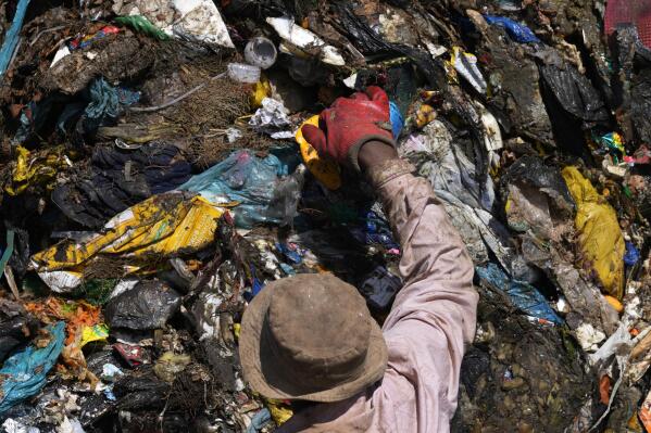 A waste picker rummages through garbage, at a dumping site in Johannesburg, South Africa, Friday, May 20, 2022. Environmental activists are gathering in South Africa this week to press governments and businesses to reduce the production of plastic because it is harming the continent's environment. (AP Photo/Themba Hadebe)
