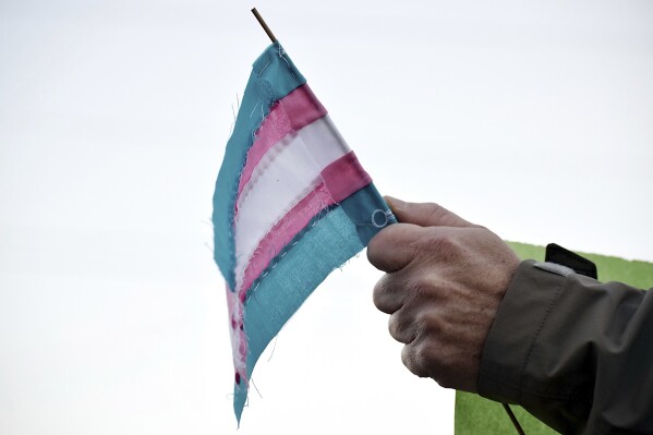 FILE - A person holds a transgender flag to show their support for the transgender community during the sixth annual Transgender Day of Remembrance at Maryville College, Nov. 20, 2016, in Maryville, Tenn. According to court documents filed Wednesday, Nov. 1, 2023, the American Civil Liberties Union and attorneys representing Tennessee transgender teens and their families have asked the U.S. Supreme Court to block a ban on gender-affirming care for minors that a lower court allowed to go into effect. (Brianna Bivens/The Daily Times via AP, File)