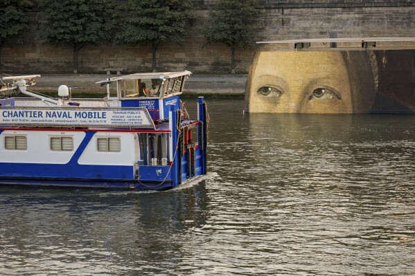 A ship sails past reproductions of artworks decorating the banks of the River Seineat the 2024 Summer Olympics, Tuesday, July 30, 2024, in Paris, France. The men's Olympic triathlon has been postponed over concerns about water quality in Paris' Seine River, where the swimming portion of the race was supposed to take place. (AP Photo/ Dar Yasin)