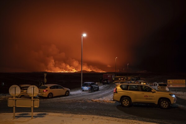 The road is blocked at the entrance of the road to Grindavík with the eruption in the background, in Grindavik on Iceland's Reykjanes Peninsula, Monday, Dec. 18, 2023. A volcanic eruption started Monday night on Iceland's Reykjanes Peninsula, turning the sky orange and prompting the country's civil defense to be on high alert. (AP Photo/Marco Di Marco)