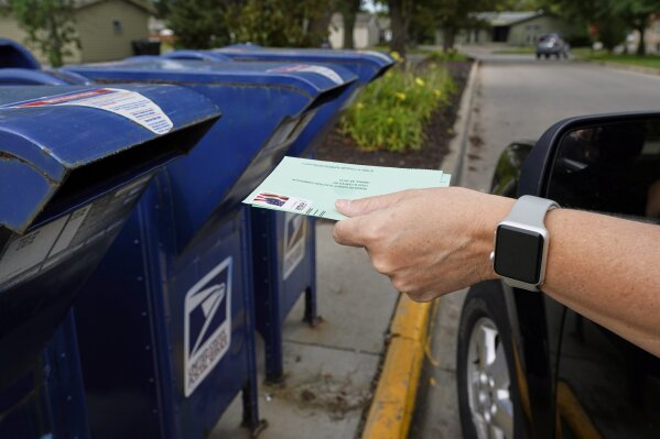 FILE - In this Tuesday, Aug. 18, 2020, file photo, a person drops applications for mail-in-ballots into a mail box in Omaha, Neb. A U.S. judge on Thursday, Sept. 17, 2020, blocked controversial Postal Service changes that have slowed mail nationwide. The judge called them "a politically motivated attack on the efficiency of the Postal Service" before the November election. (AP Photo/Nati Harnik, File)