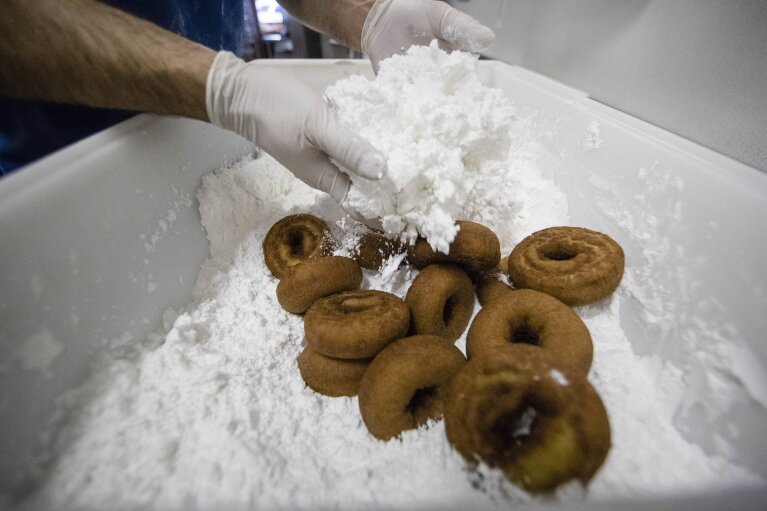 
              In this Wednesday, July 26, 2017 photo, Chef Matt Fein applies powder sugar to donuts for a Phish concert, at Federal Donuts in Philadelphia. Doughnuts are everywhere in Phish’s “Baker’s Dozen” 13-show residency at Madison Square Garden, which kicked off last week and lasts until Aug. 6. From the tickets to a huge mural to the thousands of Federal Donuts being given out to fans each night. The band is even working each night’s custom flavor into its setlists. (AP Photo/Matt Rourke)
            
