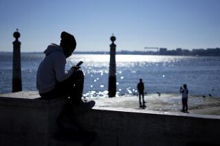 A young man checks his phone by the Tagus river at Lisbon's Comercio square on a sunny winter day, Monday, Jan. 30, 2023. (AP Photo/Armando Franca)