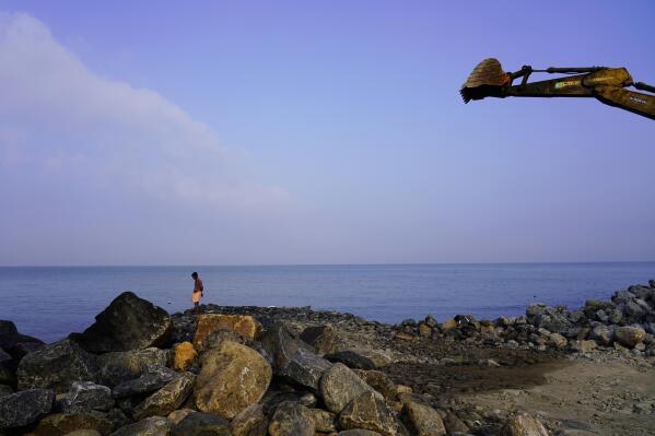 A man stands on the shore of the Arabian Sea near a digger that's part of a construction site for a new sea wall in the Chellanam area of Kochi, Kerala state, India on March 3, 2023. Tens of millions of people in India live along coastlines and thus are exposed to major weather events. (AP Photo)