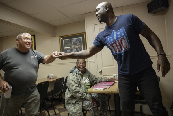 Boo Williams fist bumps a fan, Frank Lossett, left, who recognized the former New Orleans Saints player while eating lunch at Two Sisters Creole Kitchen in Picayune, Miss., Wednesday, Nov. 15, 2023. Williams needs surgery, medicine and doctors to make the pain subside from injuries he endured during his football career. But he can't afford any of it. The 44-year-old was recently awarded $5,000 a month by the NFL's disability benefit plan. But Williams said the plan and the league have repeatedly mishandled his claims and should really have paid him $500,000 or more over the past 14 years. (AP Photo/Christiana Botic)