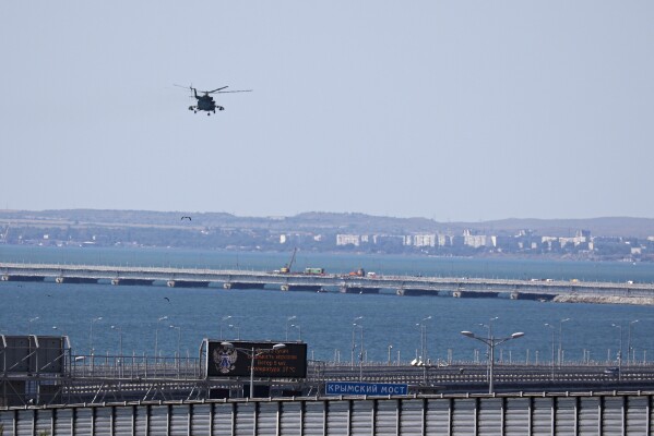 A Russian military helicopter flies over damaged parts of an automobile link of the Crimean Bridge connecting Russian mainland and Crimean peninsula over the Kerch Strait not far from Kerch, Crimea, on Monday, July 17, 2023. An attack before dawn damaged a part of a bridge linking Russia to Moscow-annexed Crimea that is a key supply route for Kremlin forces in the war with Ukraine. The strike Monday has forced the span's temporary closure for a second time in less than a year. (AP Photo)