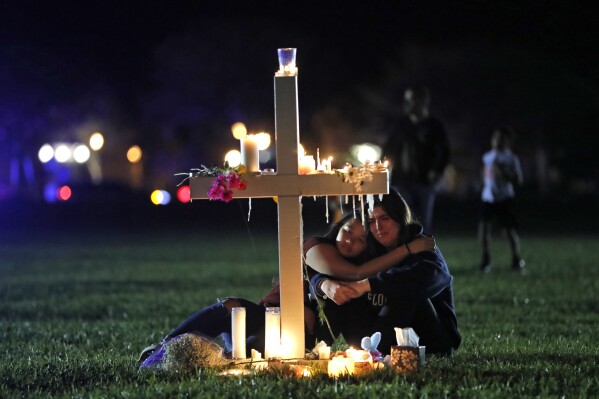 FILE - People comfort each other as they sit and mourn at one of seventeen crosses, Feb. 15, 2018, after a candlelight vigil for the victims of the shooting at Marjory Stoneman Douglas High School, in Parkland, Fla. A reenactment of the 2018 massacre that left 17 dead, 17 wounded and hundreds emotionally traumatized, is scheduled to be conducted Friday, Aug. 4, 2023, as part of lawsuits filed by the victims' families and the injured. (AP Photo/Gerald Herbert, File)