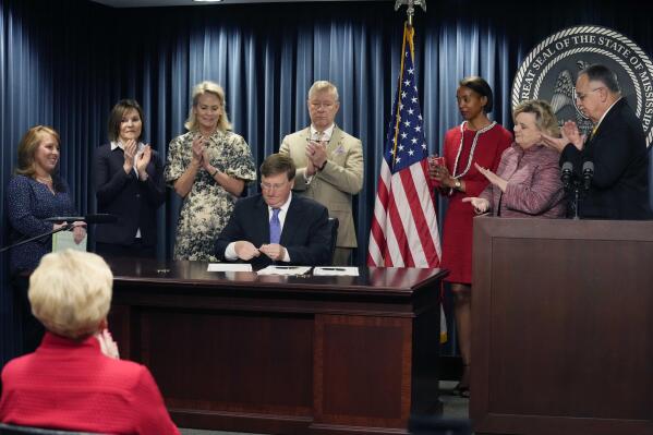 Mississippi Gov. Tate Reeves is surrounded by applauding lawmakers and others as he signs bills that are intended to improve the foster care system, speed up adoptions and provide tax credits for donations to pregnancy resource centers on Wednesday, April 19, 2023, at a state office building in Jackson, Miss. (AP Photo/Rogelio V. Solis)