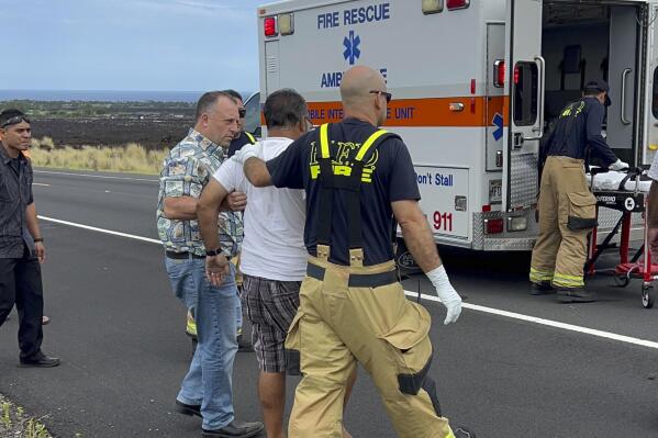 Hawaii Gov. Josh Green, second left, assists an injured driver at the scene of an overturned vehicle in Waikoloa, Hawaii, Thursday, May 18, 2023. Gov. Green, who is also a physician, was one of the people who stopped to help when his security detail spotted a vehicle upside down in a lava field Thursday while en route to a Big Island event. The man who was wearing a seatbelt, had a few cuts and bruises and seemed to be OK, Green said. (Reece Kainoa Kilbey/Office of the Governor, State of Hawai'i via AP)