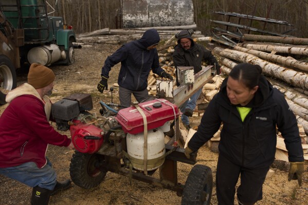 Workers with the Sustainable Energy for Galena, Alaska, from left, James Strong, Nathan Moses, Morris Demoski and Marissa McCarty move a log splitting machine before cutting wood to deliver to elders in the community Monday, May 19, 2025, in Galena. (AP Photo/John Locher)